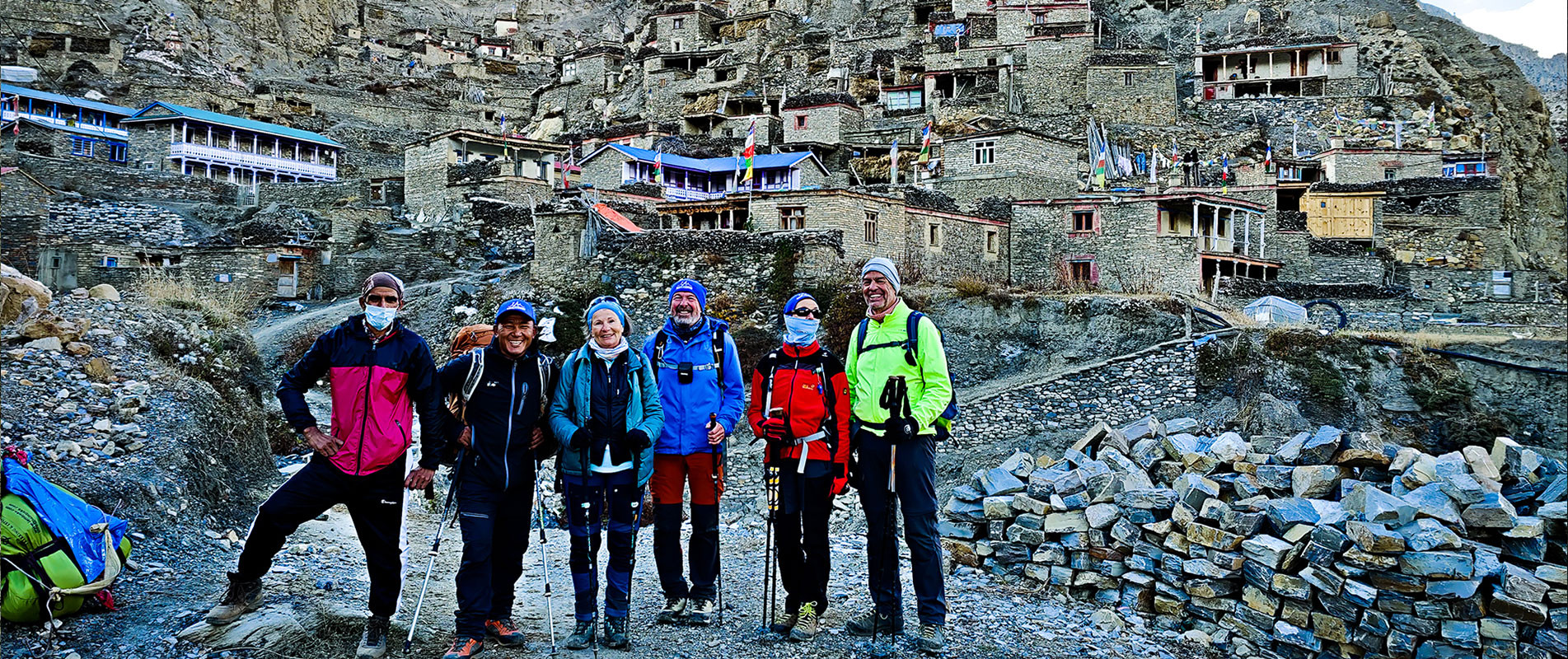 6 trekkers in Phu village with traditional stone houses behind them on the Naar Phu trek.